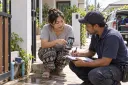 A homeowner shows a repair technician a leak photo while they discuss a quote request.