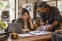 A repair-company owner takes a customer call while a technician reviews job photos and a paper quote form.