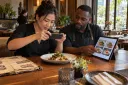 Restaurant staff photograph a dish for the digital menu beside a worn paper menu.