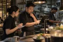 A chef checks a digital order with a server and chooses the cooking sequence himself.